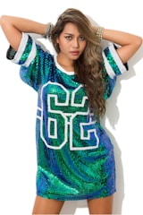 A person is wearing a sequined dress with the number 86 on the front. The dress is predominantly green and blue with sparkly sequins, and the person has long, wavy hair. They have an arm raised above their head and are wearing multiple bracelets.