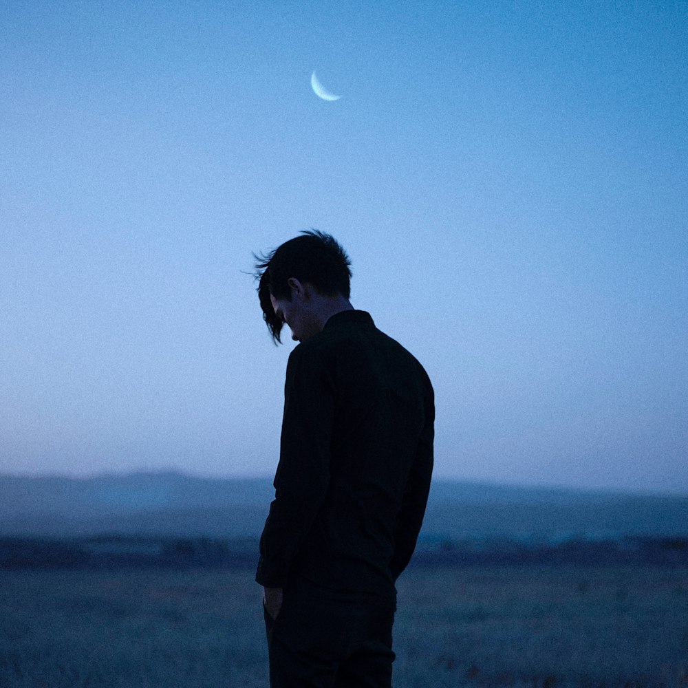 a man standing in a field with a half moon in the sky