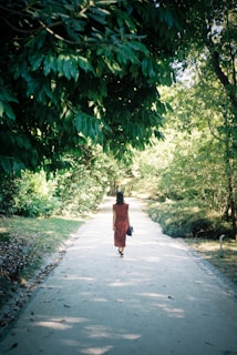 A serene outdoor scene with a model in a flowing dress walking along a sunlit path