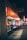 A nighttime street view featuring a series of small shops. The near shop has a bright orange awning with the text 'A J International Mall' on a sign above the store. The shops are illuminated from within, and the street is dimly lit with a few lights visible further in the distance.