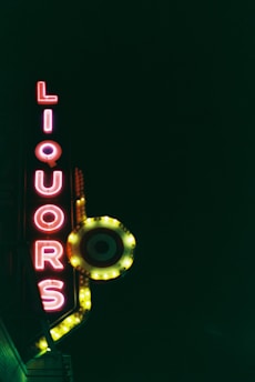 A neon sign displays the word 'LIQUORS' vertically, with glowing red and yellow colors reflecting against a dark background. A circular, target-style logo is also illuminated, adding a vintage or retro feel.
