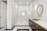 A luxurious bathroom features a large glass shower enclosure with gold fixtures. The walls are covered in white marble tiles, and the floor has a black and white marble pattern. A stylish vanity with a gold basin and round mirror complements the elegant design. Warm lighting enhances the sophisticated ambiance.