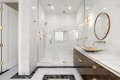 A luxurious bathroom features a large glass shower enclosure with gold fixtures. The walls are covered in white marble tiles, and the floor has a black and white marble pattern. A stylish vanity with a gold basin and round mirror complements the elegant design. Warm lighting enhances the sophisticated ambiance.