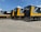 Several large black and yellow logistics trailers are parked in a lot under a clear blue sky. The trailers have bold patterns and the words 'Bros Log' displayed prominently on their sides. A small staircase is next to one of the trailers.