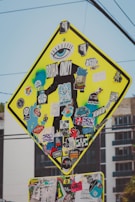 A street sign is heavily covered with a variety of colorful, overlapping stickers. The stickers feature numerous designs, including logos, graphics, and text such as 'BRUHA ONLY' and 'SK8 ONE'. The sign's original purpose is obscured, with stickers and graffiti adding a vibrant and eclectic aesthetic.