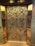 Intricately designed elevator doors feature a detailed floral and geometric pattern. The metallic surface reflects light, highlighting the elaborate engravings of large flowers with petals and swirling patterns.