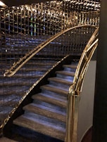 A staircase with luxurious features including glass and gold handrails, complemented by reflective wall panels that create a rich, elegant ambiance.