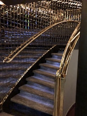 A staircase with luxurious features including glass and gold handrails, complemented by reflective wall panels that create a rich, elegant ambiance.
