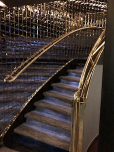 A staircase with luxurious features including glass and gold handrails, complemented by reflective wall panels that create a rich, elegant ambiance.