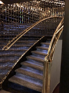 A staircase with luxurious features including glass and gold handrails, complemented by reflective wall panels that create a rich, elegant ambiance.