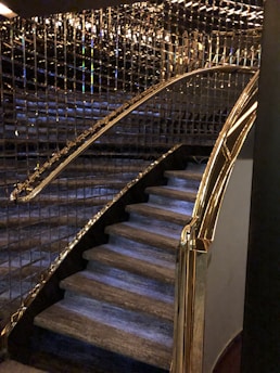 A staircase with luxurious features including glass and gold handrails, complemented by reflective wall panels that create a rich, elegant ambiance.