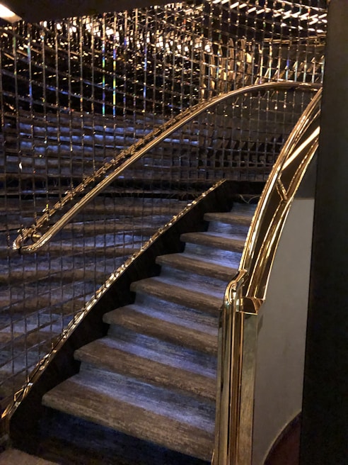 A staircase with luxurious features including glass and gold handrails, complemented by reflective wall panels that create a rich, elegant ambiance.