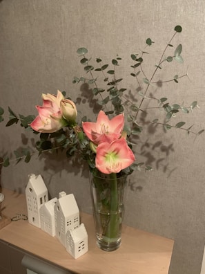 Bright pink and white blossoms in a minimalist glass vase on a rustic wooden shelf.