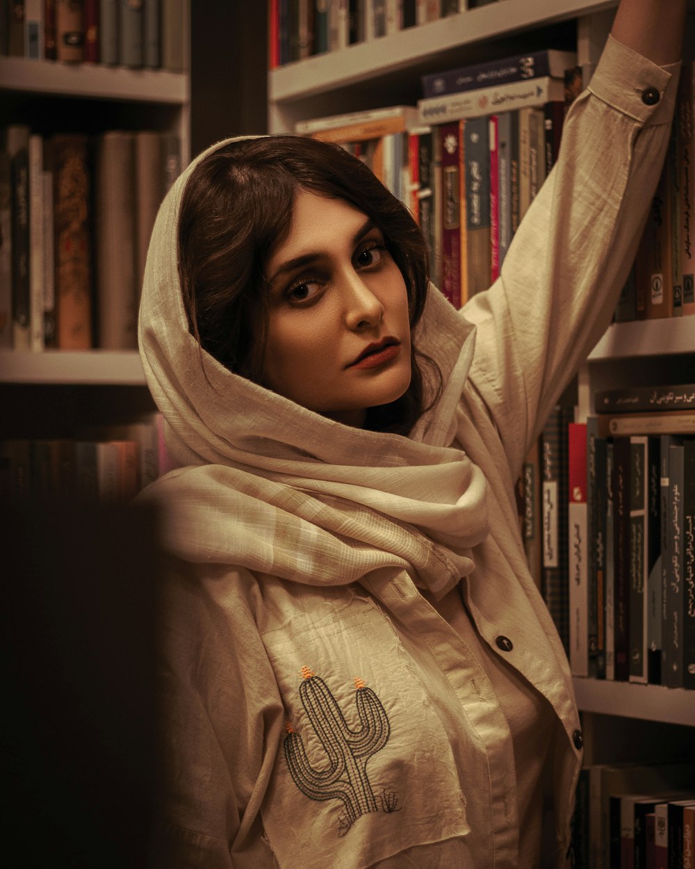a woman with a scarf around her head standing in front of a bookshelf