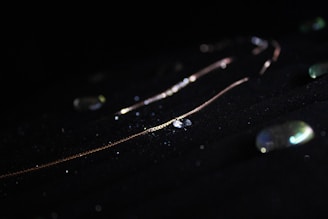 A delicate gold chain illuminated against a dark background with scattered, glittering stones.