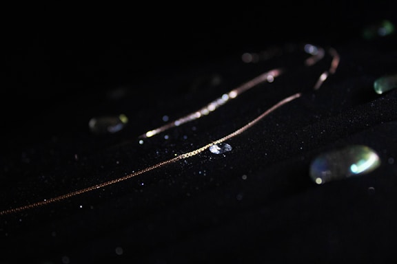 A close-up of a delicate Casso Aurora necklace glowing softly against a dark background.