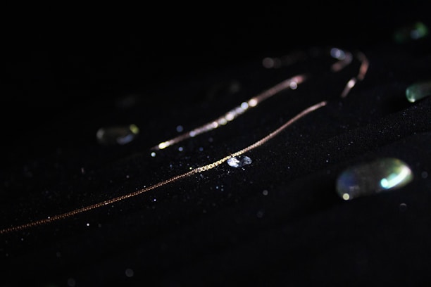 A delicate gold chain illuminated against a dark background with scattered, glittering stones.
