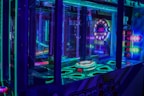 A brightly lit arcade game machine featuring neon lights and colorful graphics. The display shows point values and bonus levels, with vibrant colors reflecting off the glass and surrounding surfaces.