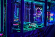 A brightly lit arcade game machine featuring neon lights and colorful graphics. The display shows point values and bonus levels, with vibrant colors reflecting off the glass and surrounding surfaces.