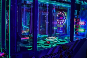 A brightly lit arcade game machine featuring neon lights and colorful graphics. The display shows point values and bonus levels, with vibrant colors reflecting off the glass and surrounding surfaces.