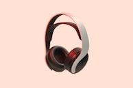 A pair of sleek, modern over-ear headphones with a white and black color scheme. The background is a solid peach color, which makes the headphones stand out prominently. The headphones have a cushioned headband and ear cups, with a red accent lighting adding a touch of elegance.