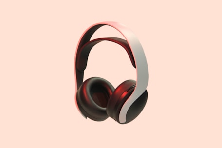 A pair of sleek, modern over-ear headphones with a white and black color scheme. The background is a solid peach color, which makes the headphones stand out prominently. The headphones have a cushioned headband and ear cups, with a red accent lighting adding a touch of elegance.