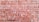 A large stack of reddish-brown bricks neatly arranged in a rectangular pattern. The surface of the bricks is textured, and some bricks have slight variations in color. There is a small gap in the arrangement where a few bricks are missing.