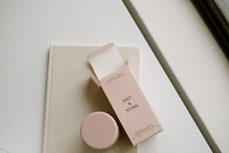 A minimalist scene with a beige-colored book or notebook, on top of which rests an open box of Salt & Stone natural deodorant gel. Next to the box is a matching container for the deodorant. The setting suggests a clean, sophisticated lifestyle.