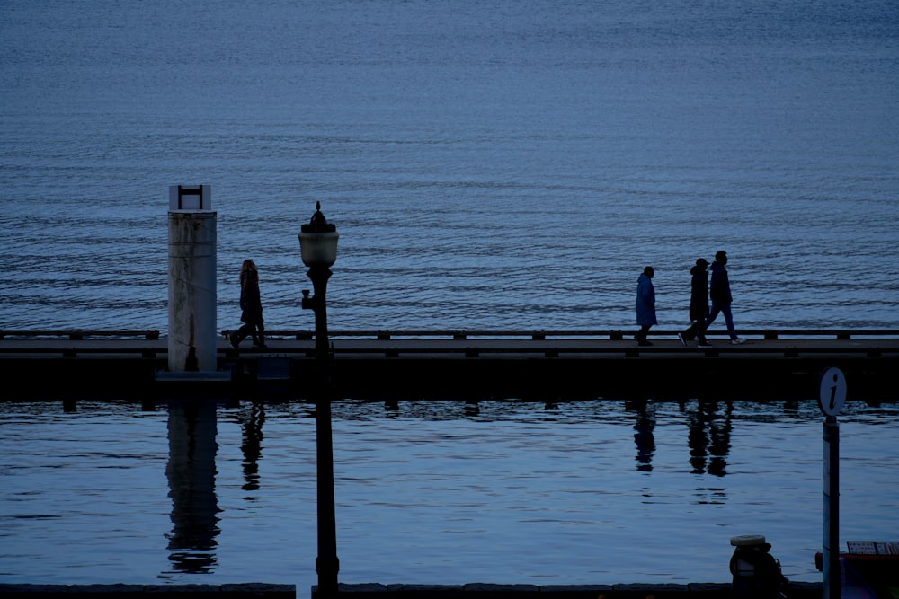 a group of people walking across a pier next to the ocean