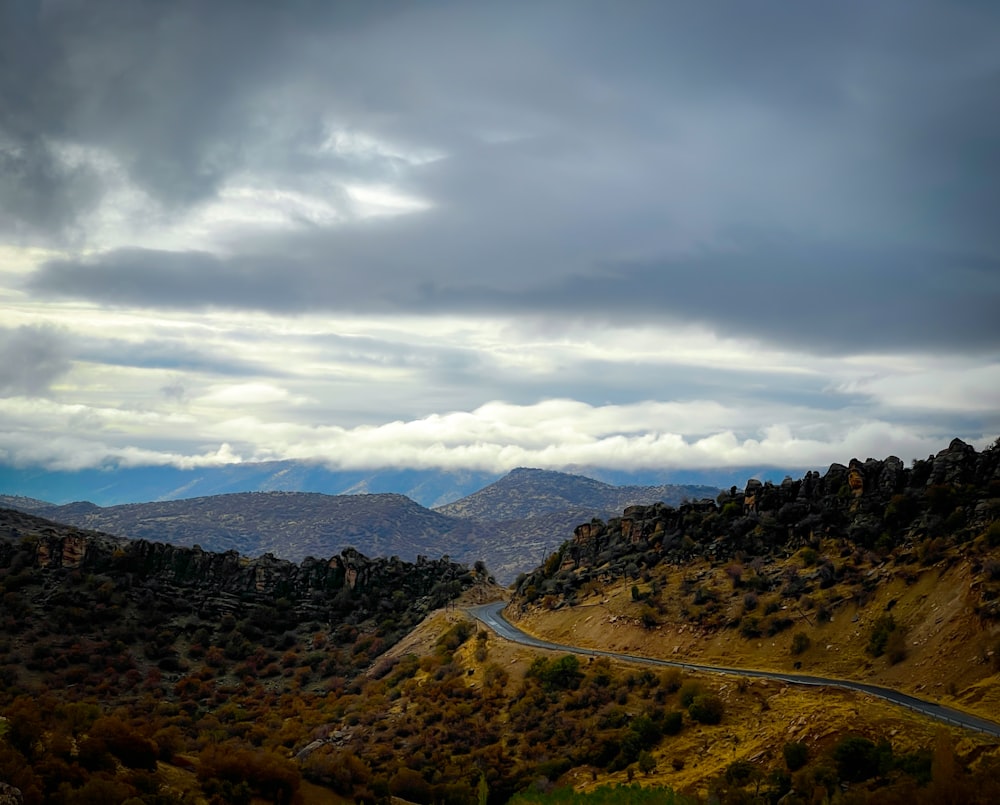 a winding road in the mountains under a cloudy sky