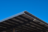 A large, angular metal roof structure set against a clear, vibrant blue sky. The roof features a grid-like pattern of beams and panels.