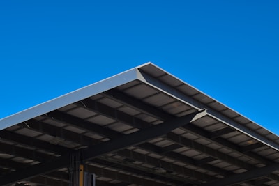 A large, angular metal roof structure set against a clear, vibrant blue sky. The roof features a grid-like pattern of beams and panels.