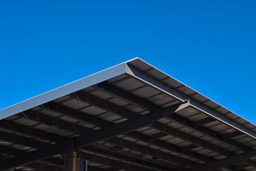 A large, angular metal roof structure set against a clear, vibrant blue sky. The roof features a grid-like pattern of beams and panels.