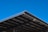 A large, angular metal roof structure set against a clear, vibrant blue sky. The roof features a grid-like pattern of beams and panels.
