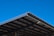 A large, angular metal roof structure set against a clear, vibrant blue sky. The roof features a grid-like pattern of beams and panels.