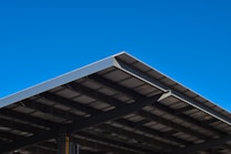 A large, angular metal roof structure set against a clear, vibrant blue sky. The roof features a grid-like pattern of beams and panels.