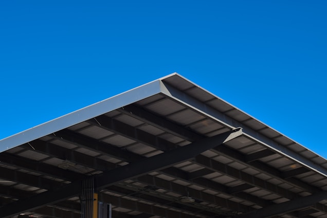A large, angular metal roof structure set against a clear, vibrant blue sky. The roof features a grid-like pattern of beams and panels.