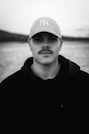 a man with a baseball cap on standing in front of a body of water