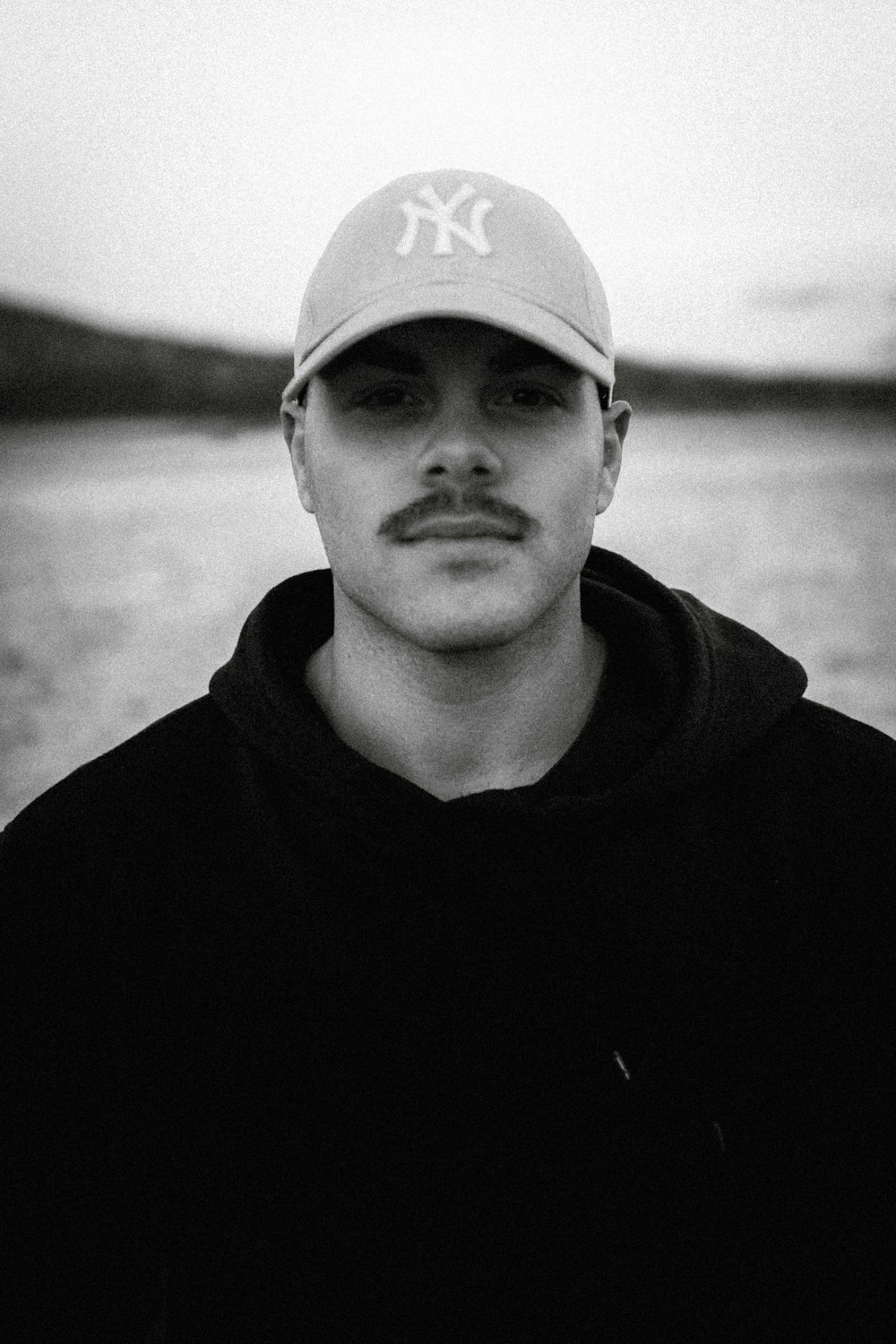 a man with a baseball cap on standing in front of a body of water