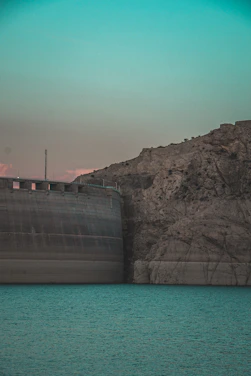 An engineer using AI software while overlooking a large dam construction site at sunset.