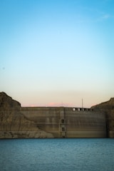 An aerial view of a large dam holding back a vast reservoir under a clear sky.