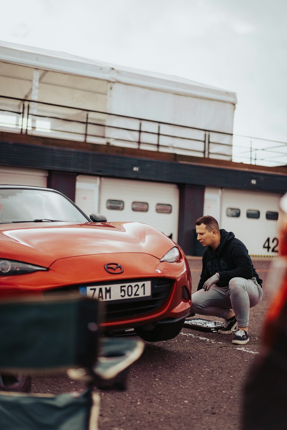 a man kneeling down next to a red sports car