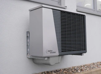 Technician installing a modern heat pump system outside a residential home on a sunny day.