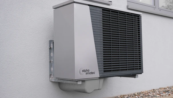 Technician installing a modern heat pump system outside a residential home on a sunny day.