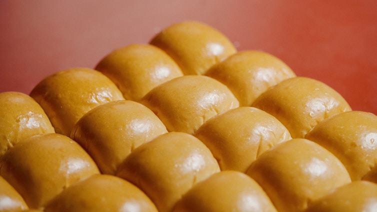Close-up of a stack of freshly baked golden buns with a soft texture, surrounded by an assortment of frozen food items on a bright red background.