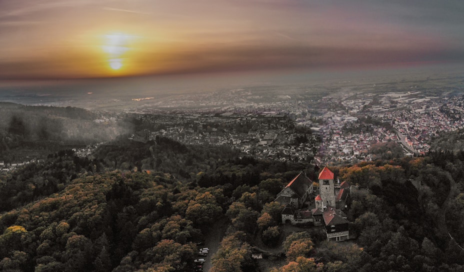 Aerial shot of a historic castle surrounded by lush greenery at sunset.