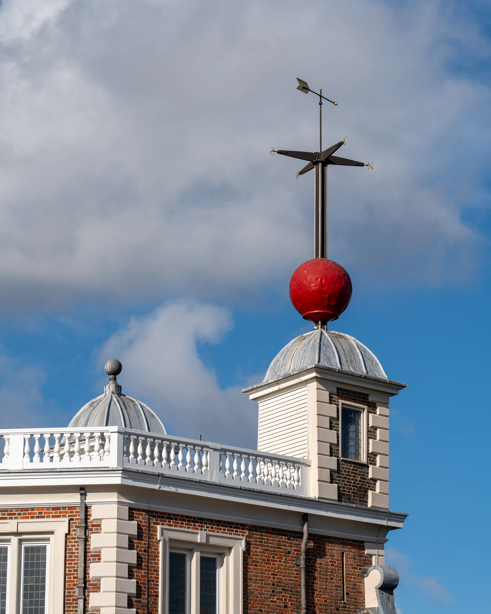 Photograph of The red time ball and weather vane stand above a white-trimmed brick building at the Royal Observatory.