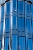 A series of reflective glass panels with a smooth, wavy design. The glass is tinted blue and features a dotted pattern across each panel, giving an impression of modern architecture.
