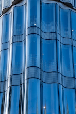 A series of reflective glass panels with a smooth, wavy design. The glass is tinted blue and features a dotted pattern across each panel, giving an impression of modern architecture.