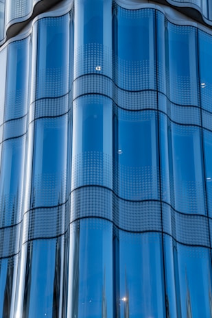 A series of reflective glass panels with a smooth, wavy design. The glass is tinted blue and features a dotted pattern across each panel, giving an impression of modern architecture.